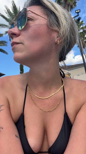Close-up of a reviewer wearing two layered gold necklaces, one a flat herringbone style, while outdoors in a black bikini top.