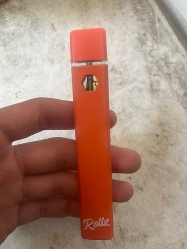 Customer holding the orange Rollz THC-A Vape in their hand against a concrete background.