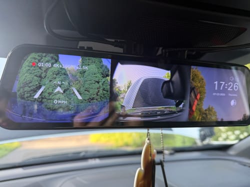 Reviewer's Wolfbox G900 TriPro dashcam mirror showing a split-screen display of the front and rear views inside their car.