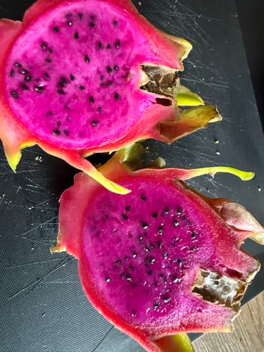 Kunde zeigt eine aufgeschnittene rote Drachenfrucht mit leuchtend pinkem Fruchtfleisch aus der Mix Box.