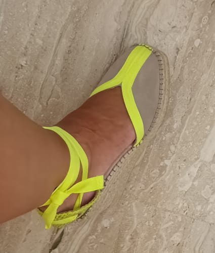 Cliente calzando una Alpargata Mara Amarillo, vista de perfil, con las tiras amarillas atadas al tobillo.