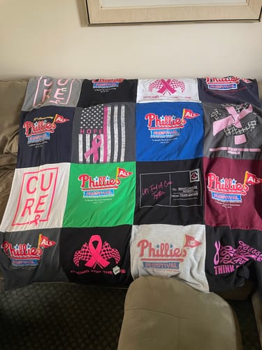 Customer's Project Repat T-Shirt Quilt made from breast cancer and ALS awareness t-shirts, spread across a couch.