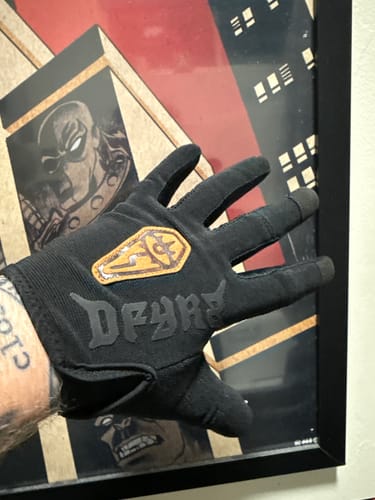 A reviewer's hand wearing the black Wraith Gravity Glove, showing the back of the glove and the logo patch.