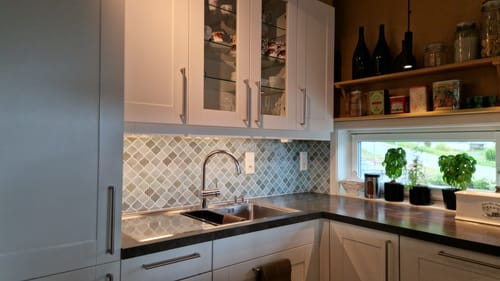 Anmelderens lanterne grønne veggfliser vist som backsplash i et kjøkken med hvite skap.