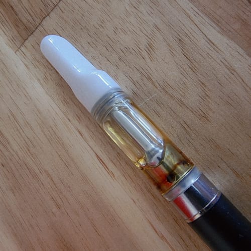 Customer's close-up of the 10-OH Cartridge with a white tip, showing the golden liquid inside on a wood surface.