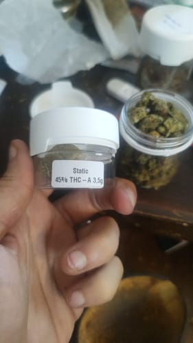 Customer holding a small jar of flowers from the CALI MIX AAA+ with another jar of buds in the background.