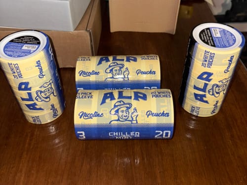 Reviewer's multiple sleeves of ALP Chilled Mint Nicotine Pouches arranged on a wooden table.