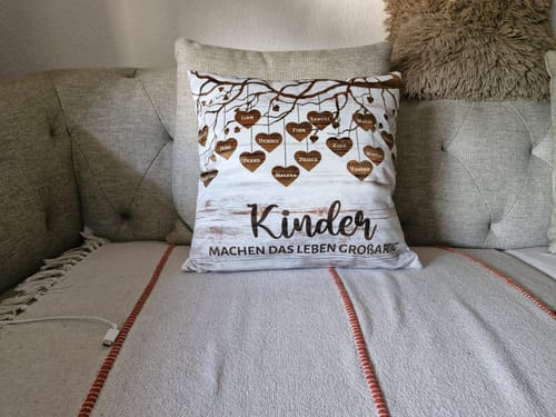 Ein Kunde zeigt sein personalisiertes Kissen mit einem Stammbaum-Design auf einem grauen Sofa.