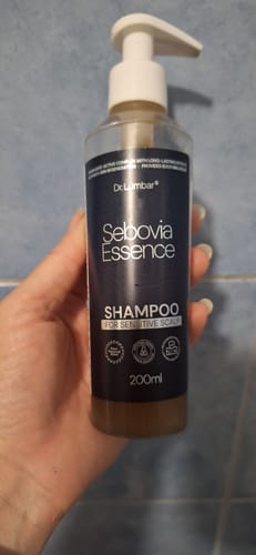 Reviewer holding a clear bottle of Dr. Lumbar Sebovia Essence Shampoo for sensitive scalp.