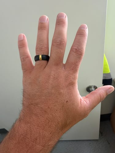 Customer's hand wearing the black Silicone Wedding Ring with a gold metal bar.