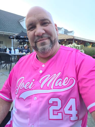 Reviewer sitting outdoors wearing the custom pink and white gradient baseball jersey with 'Joei Mae' and '24' on the front.