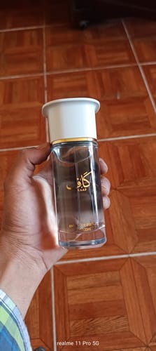 Reseñador sosteniendo la botella de cristal del perfume KAAF con tapa blanca y detalles dorados.