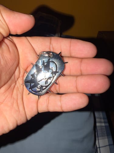 Reviewer holding the exclusive silver-toned pendant with a spiked edge in their open palm.
