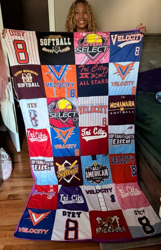 Reviewer holding up their colorful Project Repat T-Shirt Quilt made from various softball jerseys.