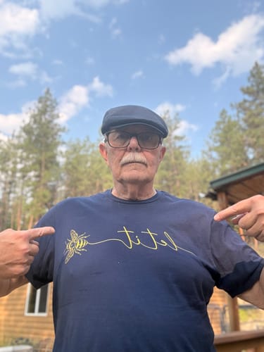 Reviewer wearing the navy Let It T-Buzz T-Shirt, pointing to the yellow bee graphic on the chest.