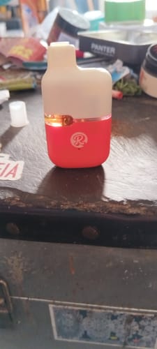 Reviewer's red and off-white THC-A Vape standing on a dark, cluttered surface.
