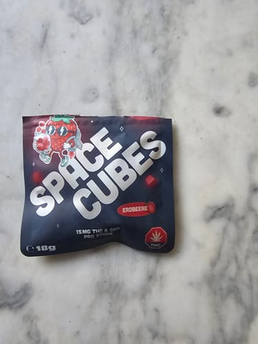 Kunde zeigt die Verpackung der Spacecubes-Probe in der Sorte Erdbeere auf einer Marmorplatte.