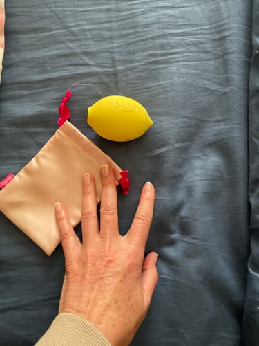 Customer placing their hand next to the yellow Lem Clitoral Massager and its pouch to show its size.