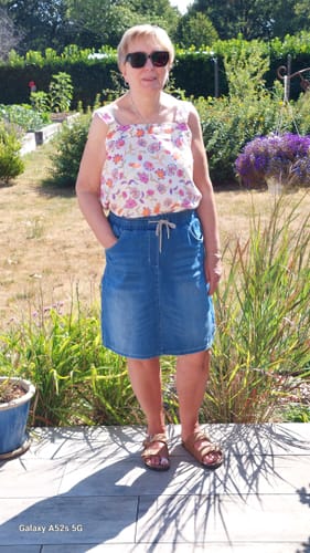 Cliente portant la Blouse Florence à motif floral avec une jupe en jean, debout à l'extérieur.