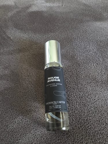 Customer's travel-size bottle of Rouge Avenue Eau de Parfum with a silver cap, lying on a grey fabric background.