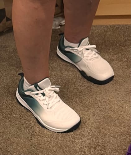 Reviewer wearing the white and green CUURT Muuv Wide Toe Box Shoes indoors on a carpet.