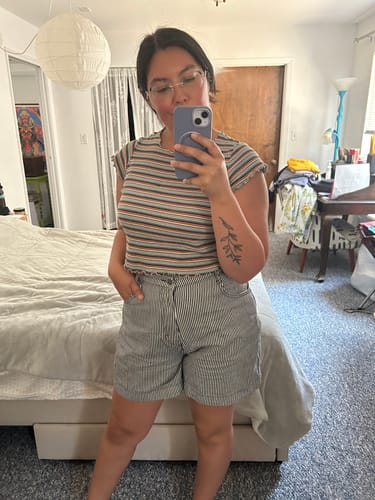 Reviewer taking a mirror selfie in a bedroom, showing the fit of the striped Utility Shorts.