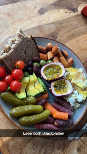 Kunde zeigt eine halbierte Bio-Passionsfrucht auf einer bunten Snackplatte.