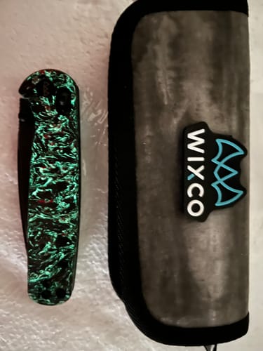 Customer's folded Wixco Drax II knife with its luminous handle glowing bright green, next to its carrying case.