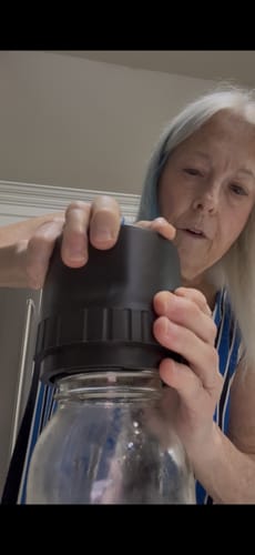 A reviewer placing the black Mason Genie Vacuum Sealer on top of an empty glass mason jar.