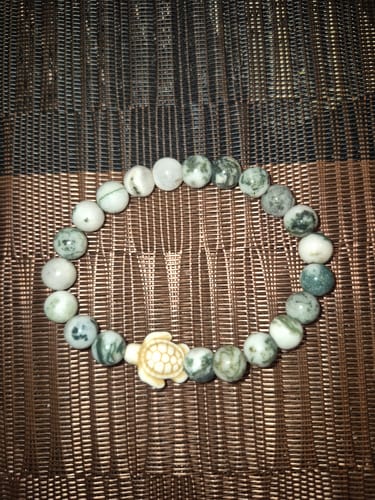 Customer's Journey Bracelet with light marbled beads and a cream-colored turtle charm on a woven surface.