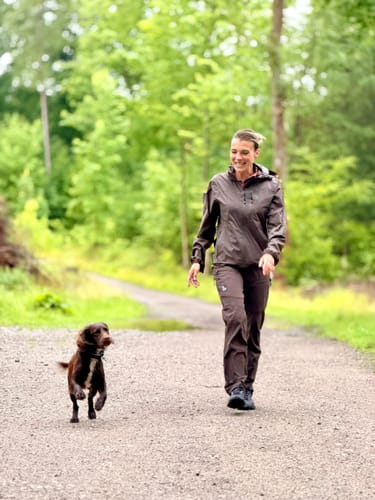 Anmelder går tur med sin hund i skoven iført den lette FeelFree Ultralight Rain Jacket i farven bison.
