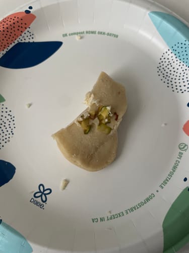 Reviewer's partially-eaten piece of Rehmat-e-Shereen Ras Malai on a paper plate, showing the creamy, nutty inside.