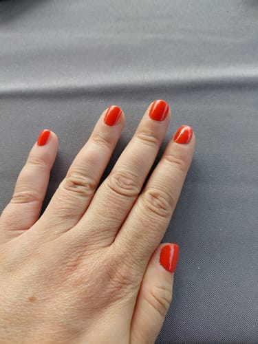 Hand einer Rezensentin mit einer Maniküre, die die glänzenden, roten 'Red Stilettos' UV-Gel-Folien auf kurzen Nägeln zeigt.