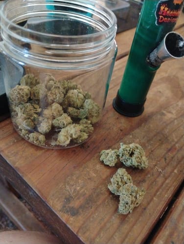 Customer's Ice Cream Cake THCA Flower in a glass jar and on a wooden table next to a green pipe.