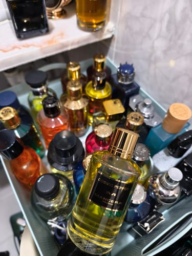 Cliente sosteniendo su perfume Mancera Cosmic Pepper frente a una extensa colección de fragancias.
