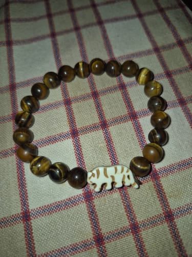 Customer's Prowl Bracelet with Tiger's Eye beads and a white tiger charm laid on a plaid surface.