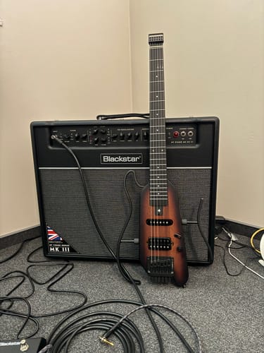 Rezensent zeigt die kopflose Donner HUSH X E-Gitarre, die an einen Verstärker angeschlossen ist und davor steht.