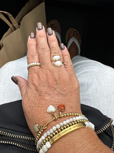 Reviewer's wrist showing several heart-shaped Coastal Charms on a gold bracelet, worn in a stack with other bracelets.