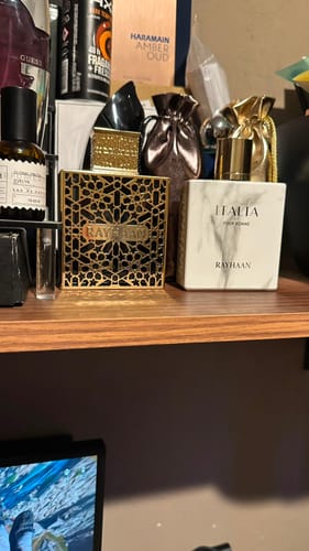 Cliente muestra su perfume Rayhaan Elixir en su caja negra y dorada en una estantería junto a otras fragancias.