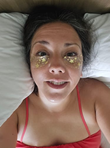 Reviewer looking calm and relaxed in bed with gold under-eye masks after taking Create Gummies.