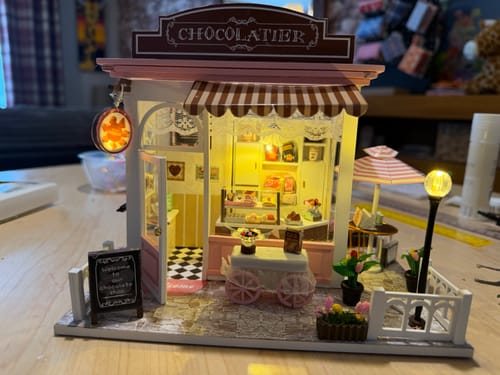 Reviewer's assembled 'The Chocolatier' miniature kit with warm LED lights illuminating the shop's detailed interior.