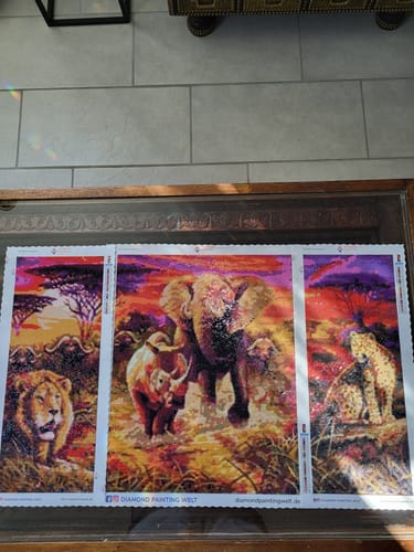 Ein Kunde zeigt das fertige dreiteilige Diamond Painting 'Big Five', das einen Löwen, einen Elefanten, ein Nashorn und einen Leoparden zeigt.