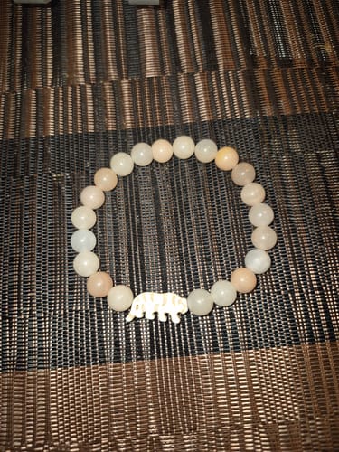 Customer's Prowl Bracelet with creamy orange beads and a tiger charm, laid on a textured surface.
