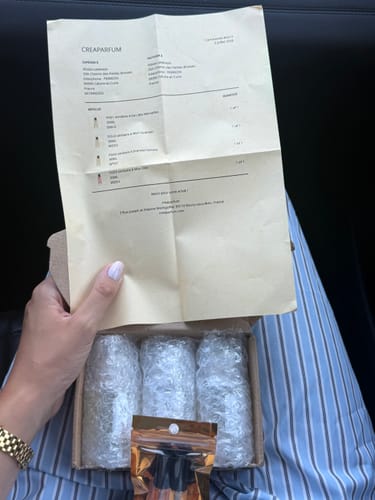 Cliente montrant le bon de commande pour le parfum FCD5 au-dessus de la boîte de livraison ouverte.