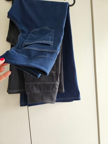 Müşterinin, askıda duran mavi ve siyah renkli Noodlab Flex Comfort Jean'lerini yakından göstermesi.