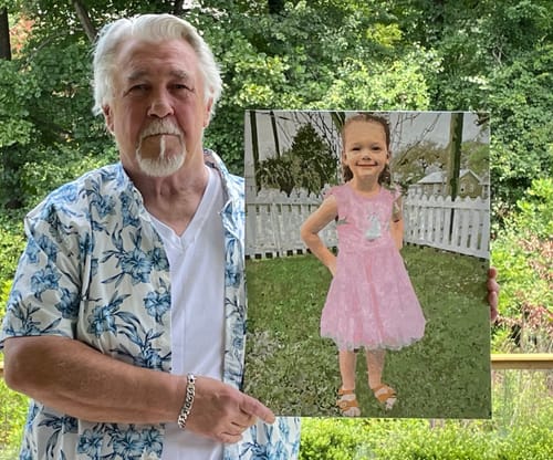 Reviewer holding a framed, realistic portrait of a young child in a pink dress on a grassy, outdoor background.