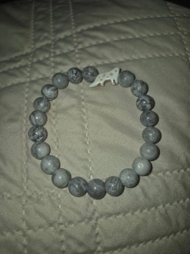 Reviewer's Ascent Bracelet with marbled grey beads and a snow leopard charm on a quilted surface.