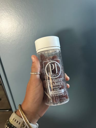 Customer's hand holding a clear, cylindrical jar of CBG Energy Gummies with cherry-colored contents.