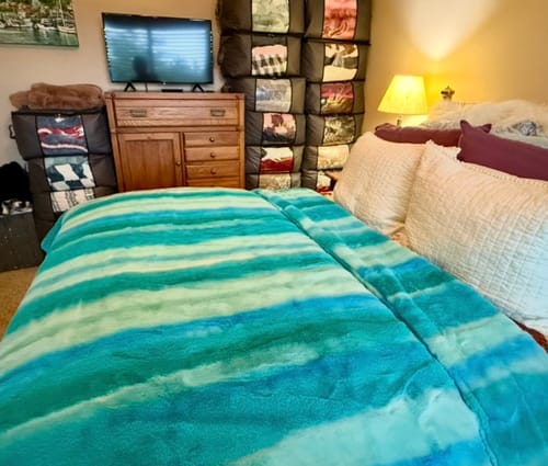 Customer's Lush Sea To Sky blanket, a soft blue-streaked plush throw, spread neatly on a bed.