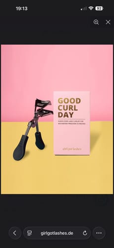 Reviewer's GOOD CURL DAY Wimpernzange neben der rosafarbenen Produktverpackung auf gelbem Hintergrund.